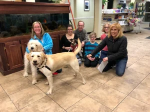 A group of six people and three dogs pose together indoors near a large fish tank and pet supply shelves.